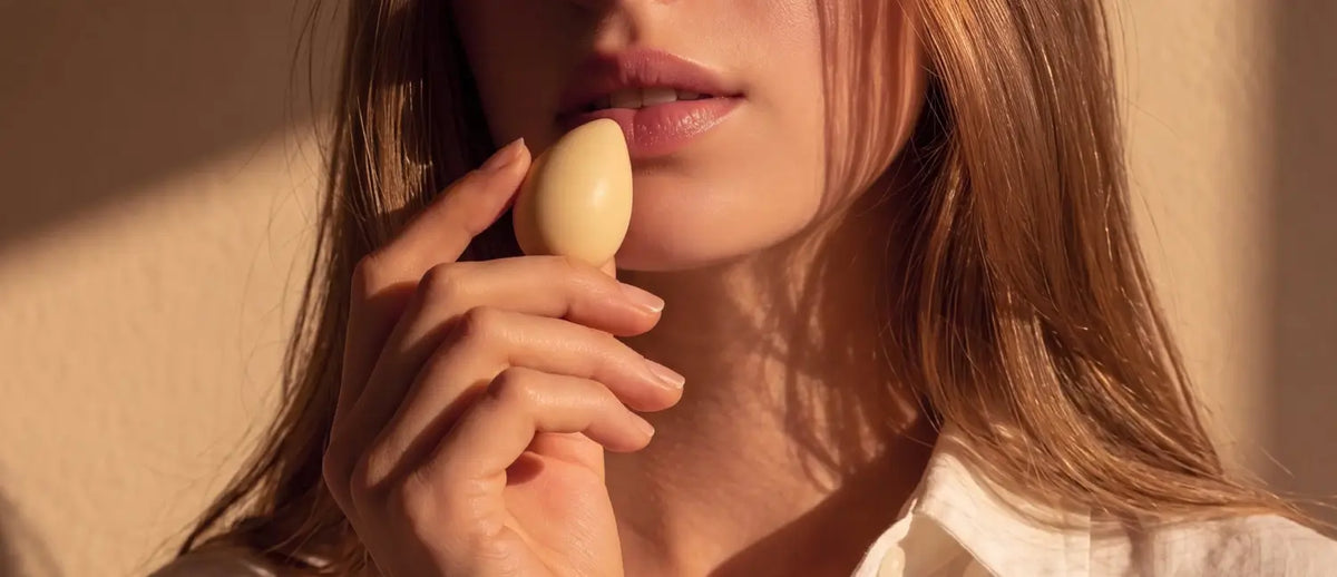 Close-up of a white chocolate teardrop praline held to the lips