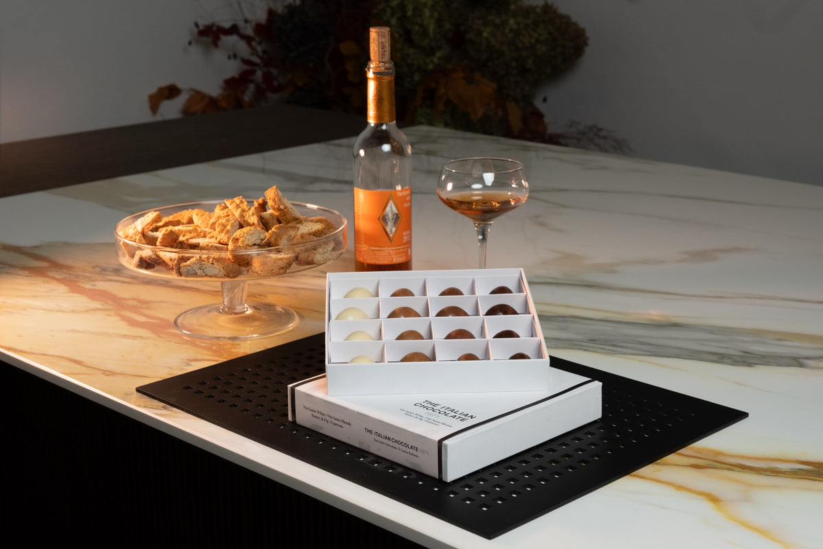 A Taste of Tuscany box of 16 pralines on a marble table with cantucci and a glass of Vin Santo