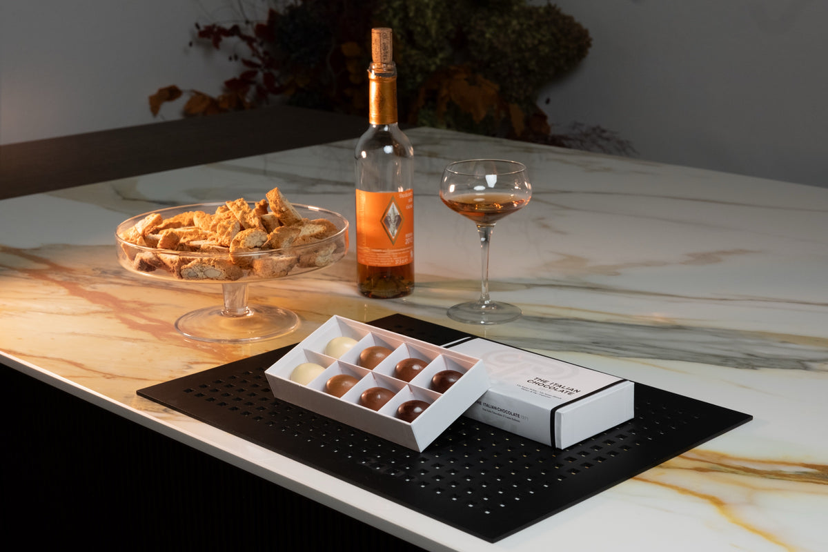A Taste of Tuscany box of 8 pralines on a marble table with cantucci and a glass of Vin Santo