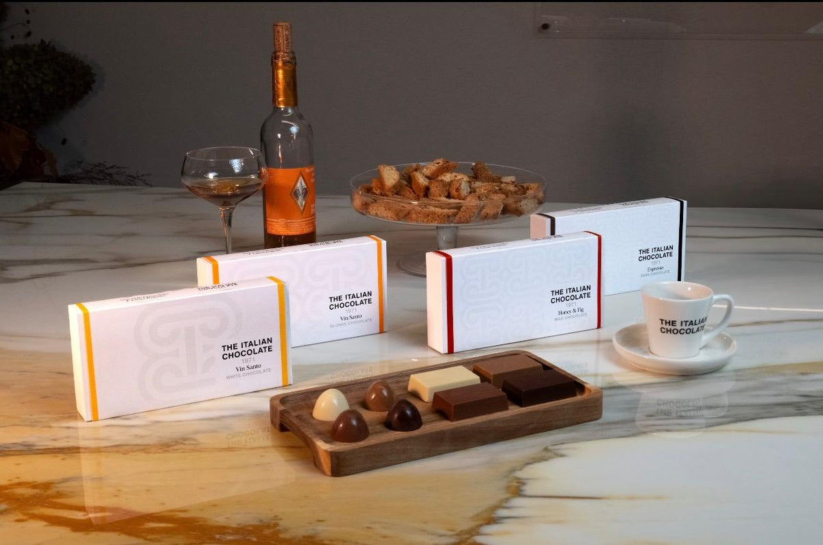 A Taste of Tuscany chocolate boxes, Vin Santo, Honey & Fig and Espresso, with pralines and bars on a walnut tray, Vin Santo, cantucci and an espresso cup on a marble table