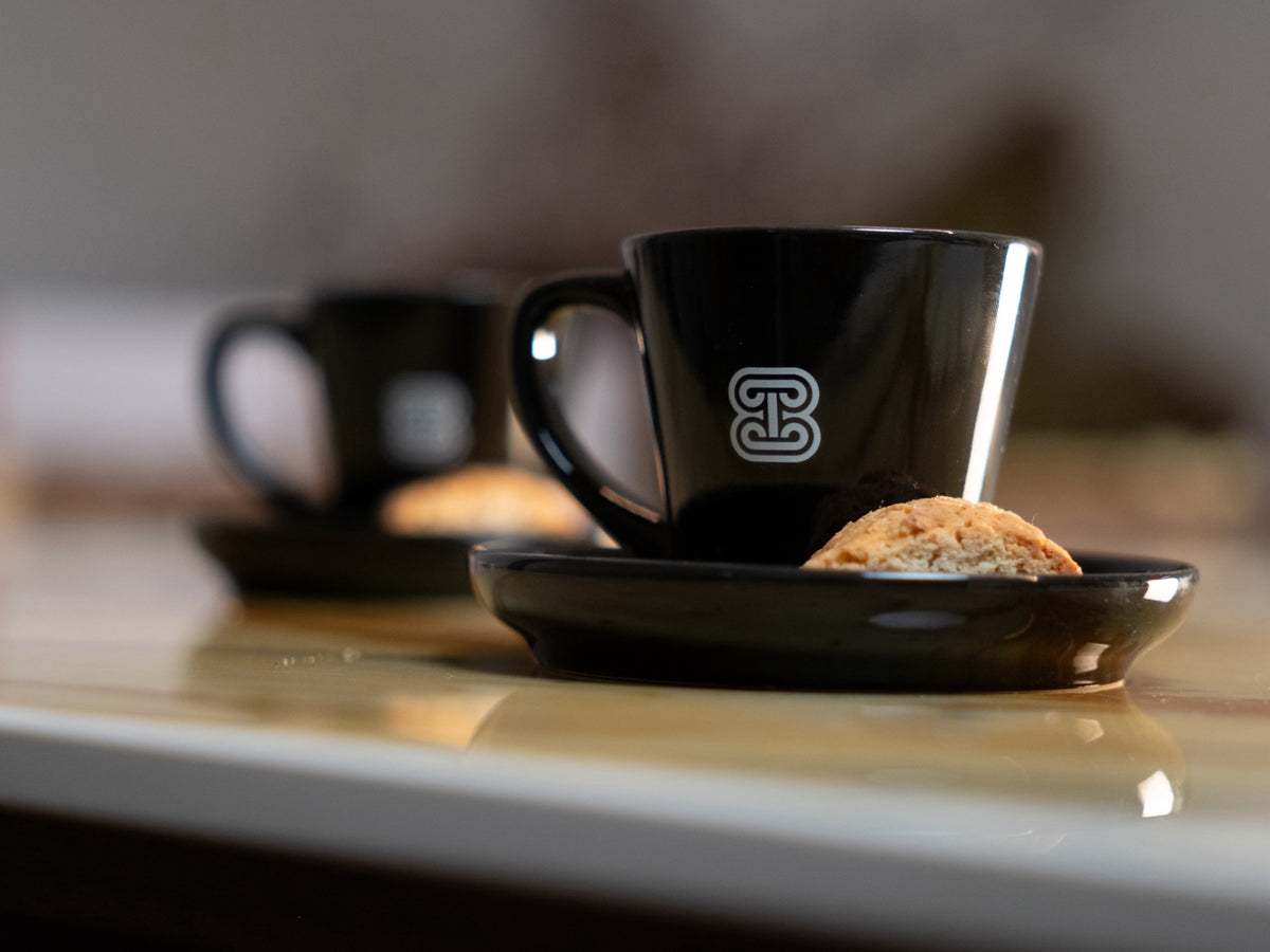 Two black espresso cups with The Italian Chocolate 1971 brandmark and almond cantucci on the marble counter at The Atelier 1971 in Florence